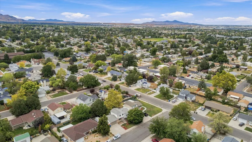 Aerial perspective showcasing a tree-lined residential neighborhood with established mature landscaping, single-family homes on spacious lots, and mountain ranges visible in the distance under clear skies