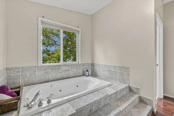 Spa-inspired primary bath featuring a sunken soaking tub with integrated jets, marble-look tile surround, and polished chrome fixtures