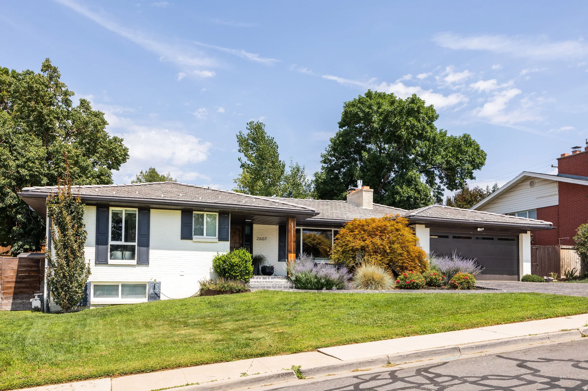 White brick exterior with dark shutters, attached two-car garage, and a lush lawn
