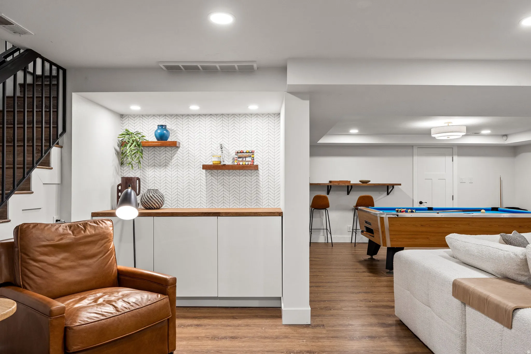 Recessed lighting, wood-finish flooring, staircase with dark iron balusters, built-in cabinetry, and chevron-patterned wall tile