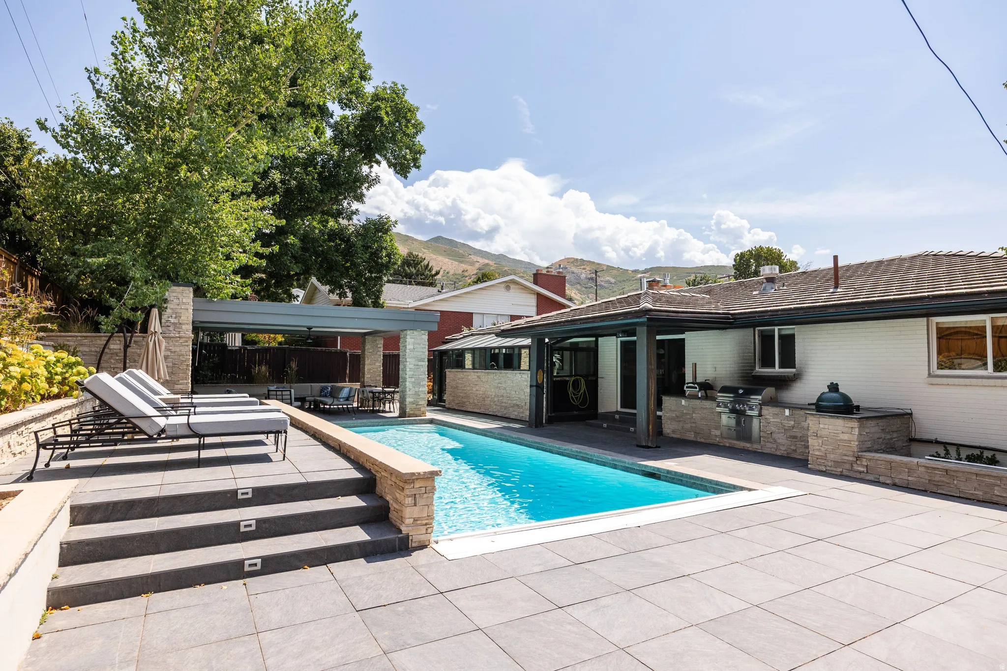 Expansive pool deck with a rectangular swimming pool, integrated outdoor kitchen with built-in grill, covered patio, and tiered hardscaping
