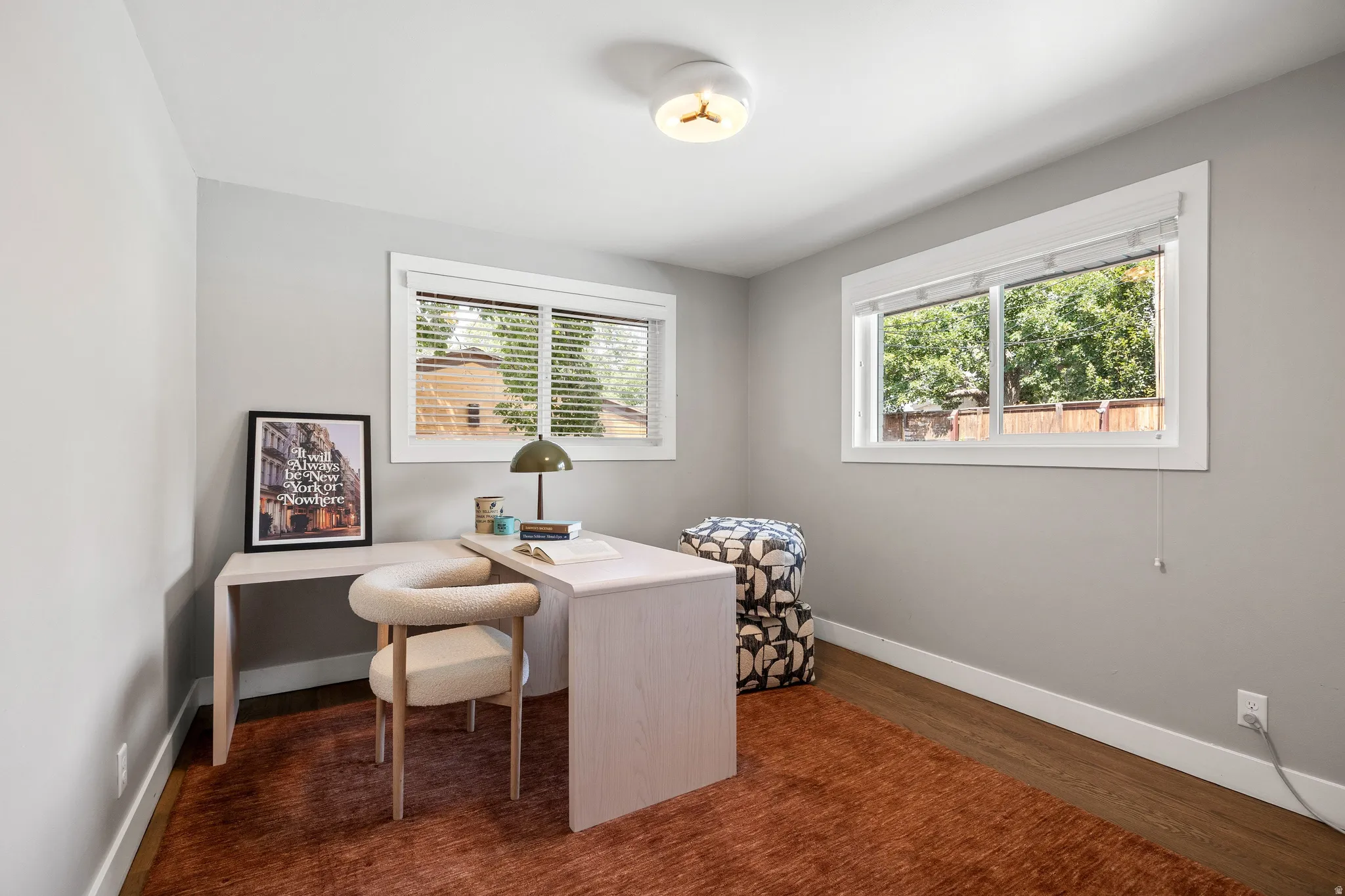 Recessed lighting, light gray walls, wood-finish flooring, two windows with white trim and blinds, and a contemporary flush-mount ceiling light