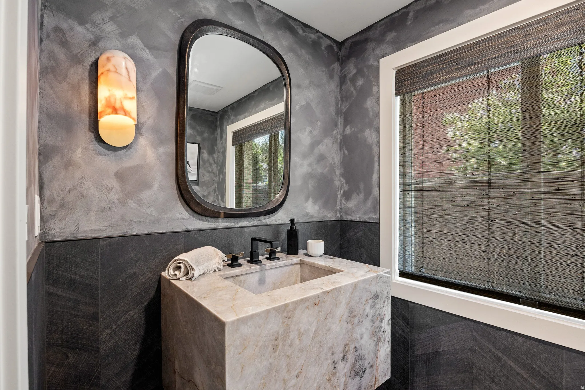Floating vanity with integrated sink, black wall-mounted faucet, custom wall sconce, framed mirror, and textured wall finish