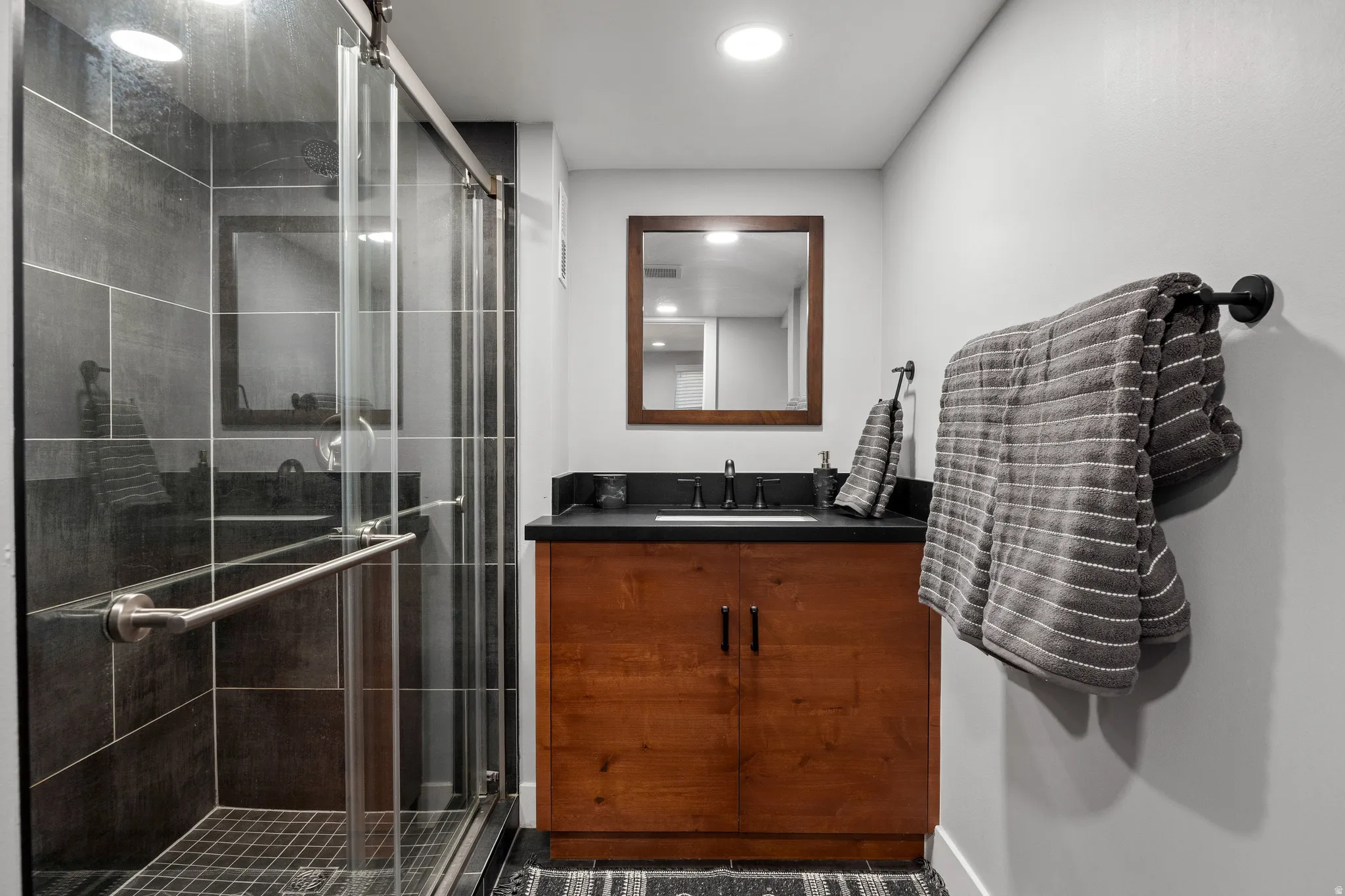 Glass-enclosed shower with dark tile surround and tiled floor
