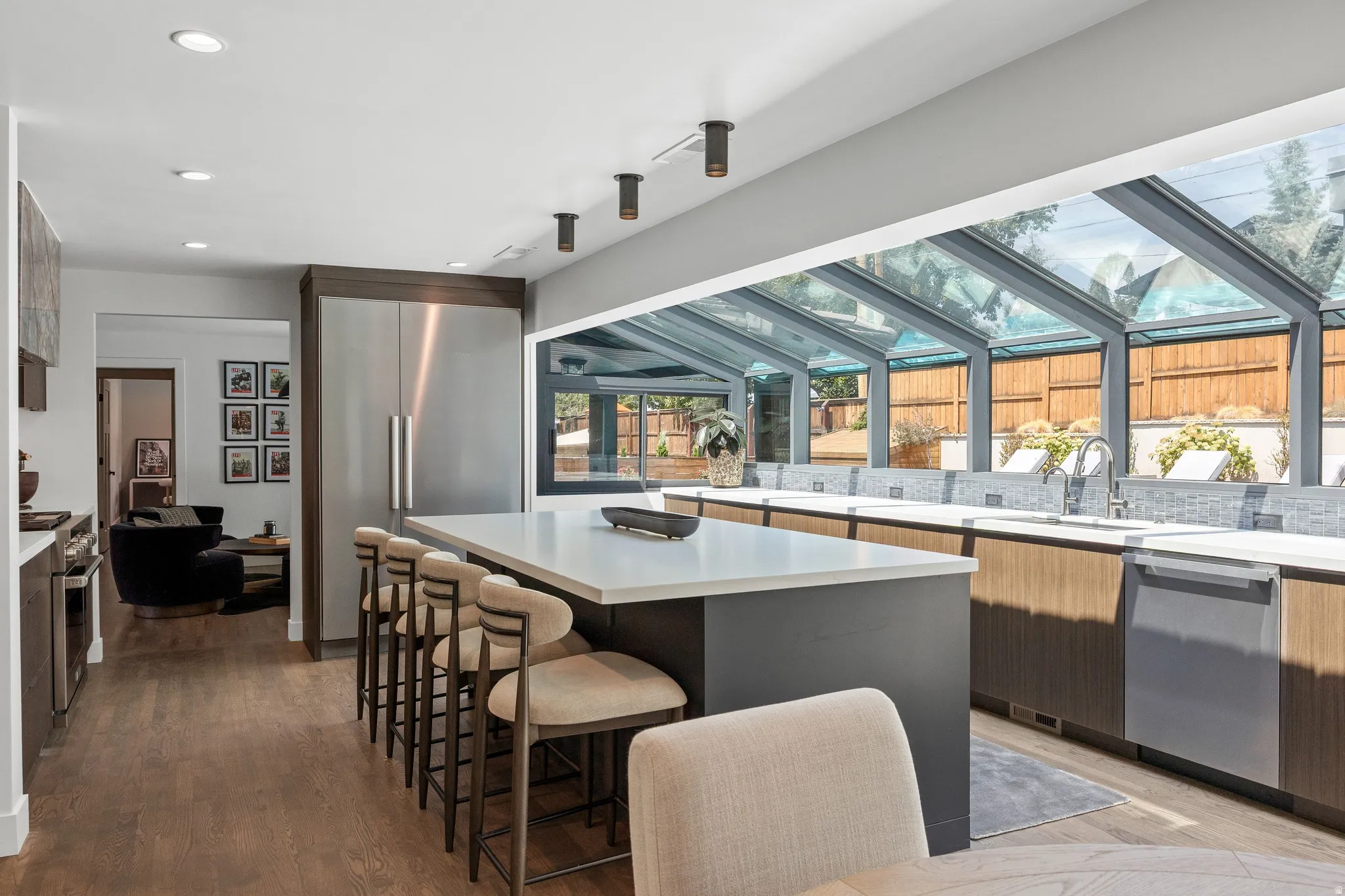 Modern kitchen featuring an expansive island with seating, stainless steel appliances, wood-finish flooring, and a glass-enclosed sunroom with a tiled backsplash