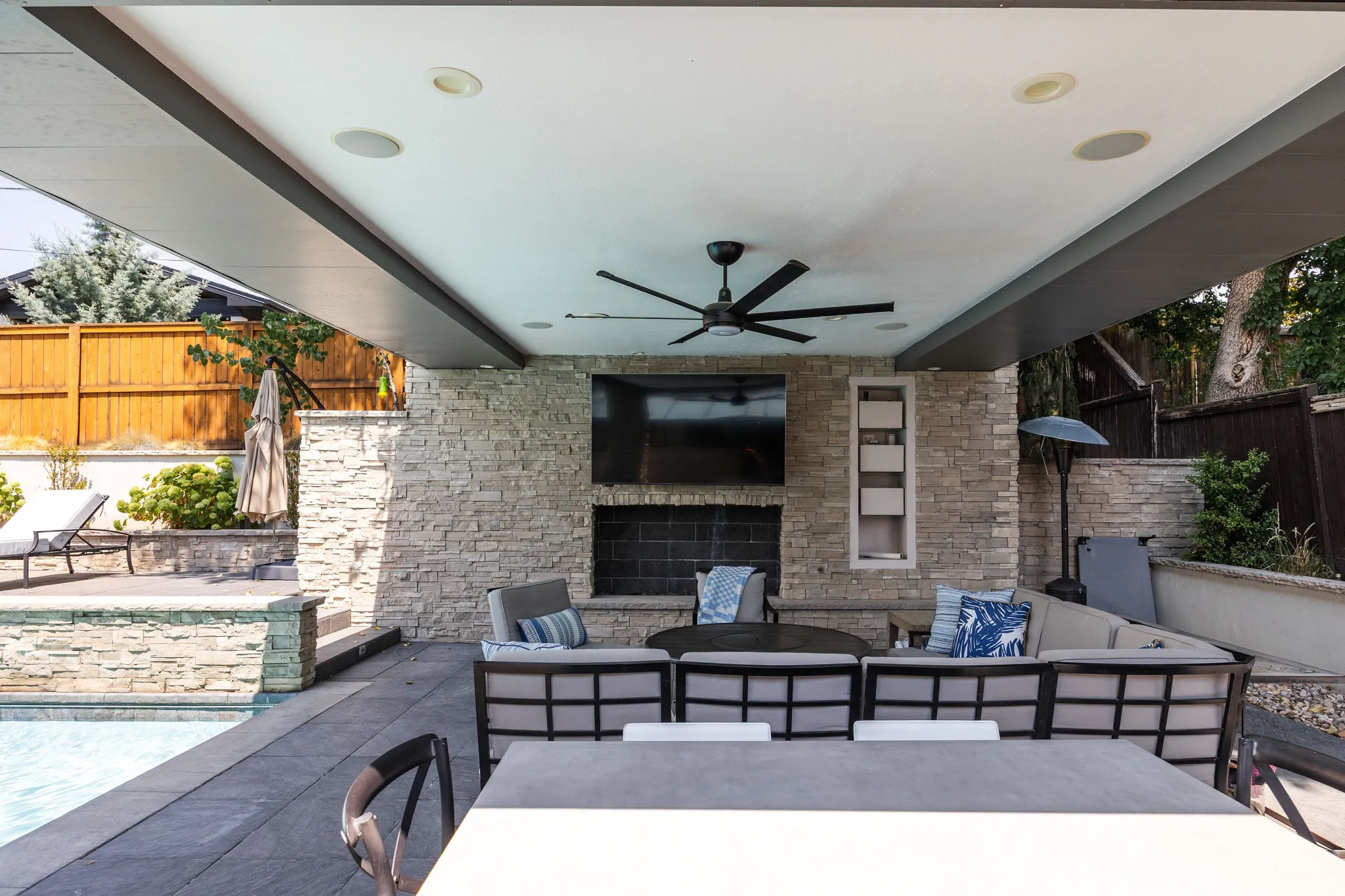 Covered patio with stacked stone wall, built-in outdoor fireplace, recessed lighting, and ceiling fan