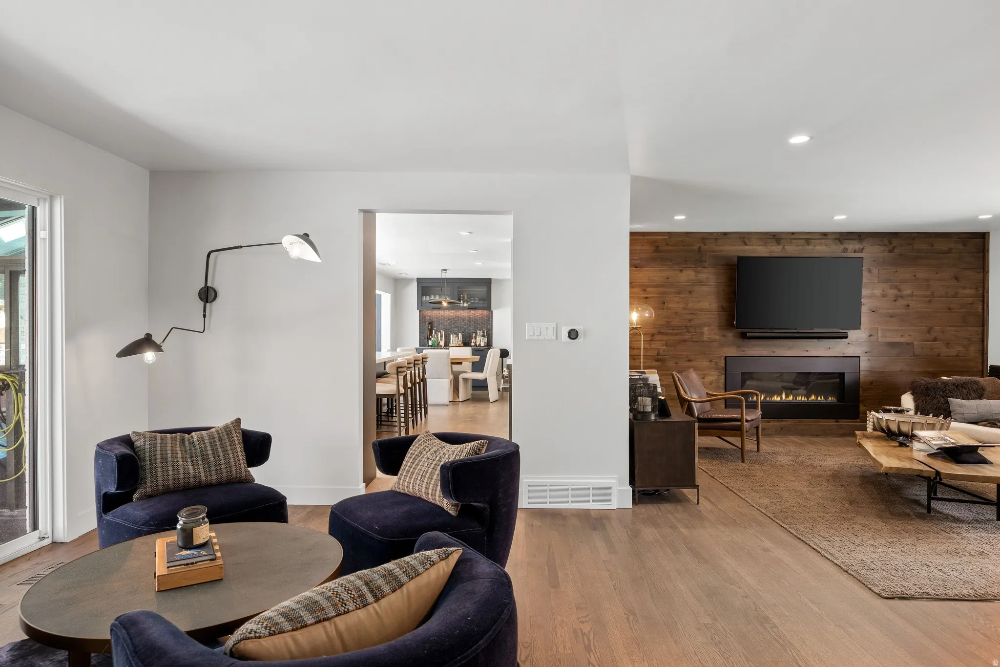 Hardwood-style flooring throughout, featuring a living area with a wood-paneled accent wall, built-in linear fireplace, and recessed lighting