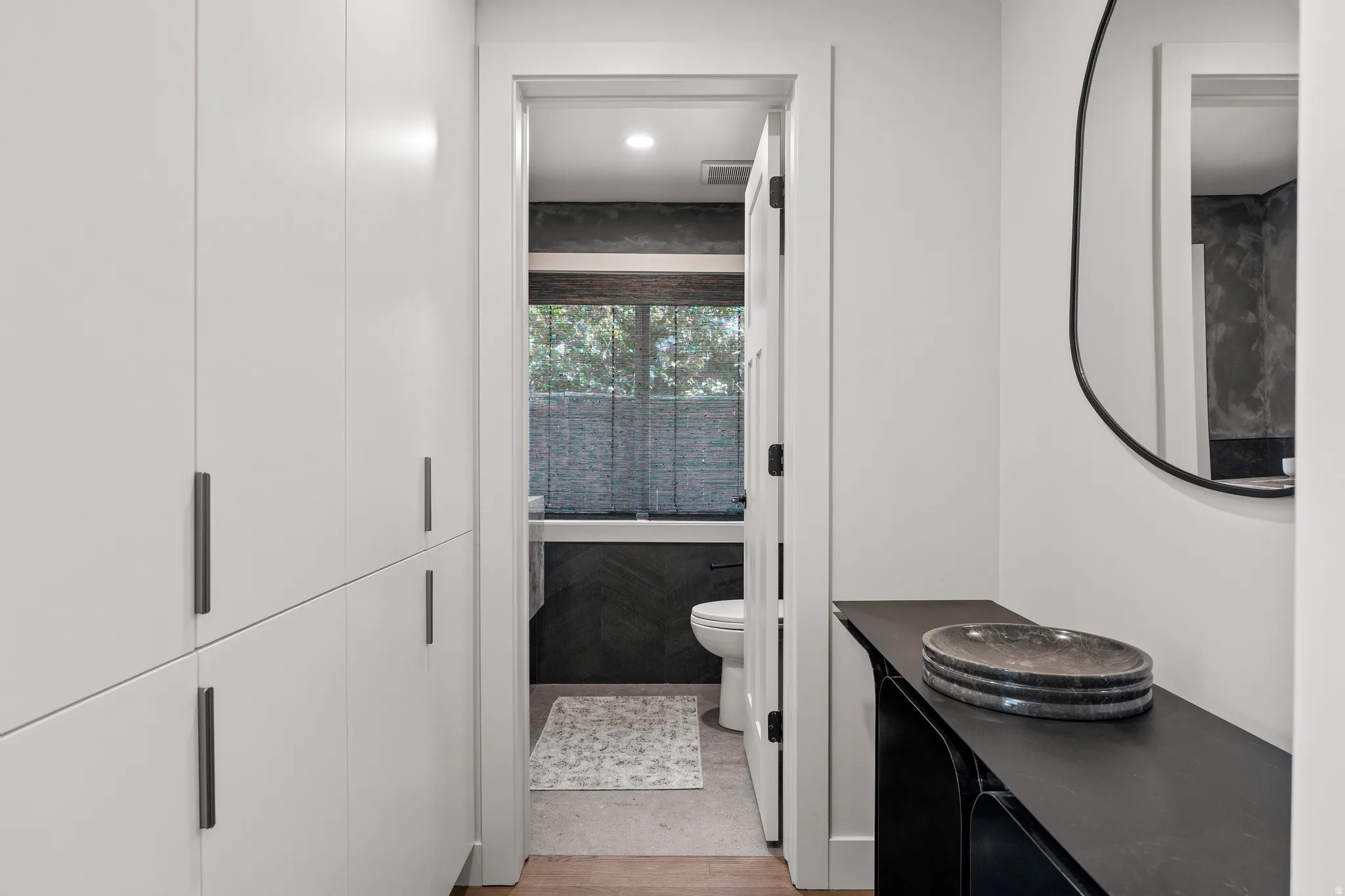 Integrated white cabinetry with dark hardware, dark floating console, and a contemporary wall mirror
