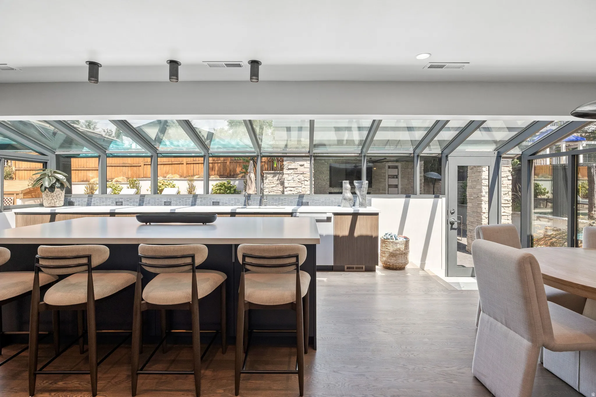 Contemporary sunroom with a glass roof, large central island with seating, dark wood-finish flooring, and recessed lighting