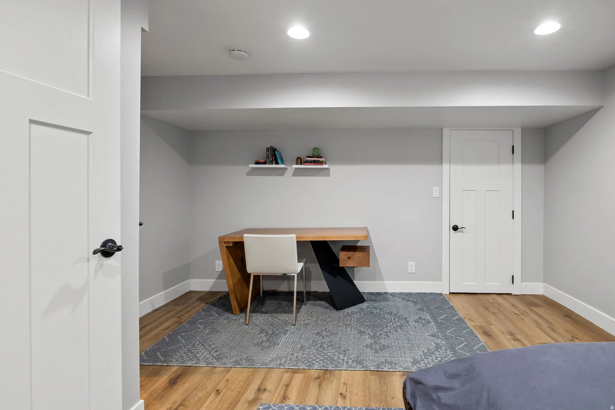 Recessed lighting illuminates wood-finish flooring, complemented by light gray walls and white trim