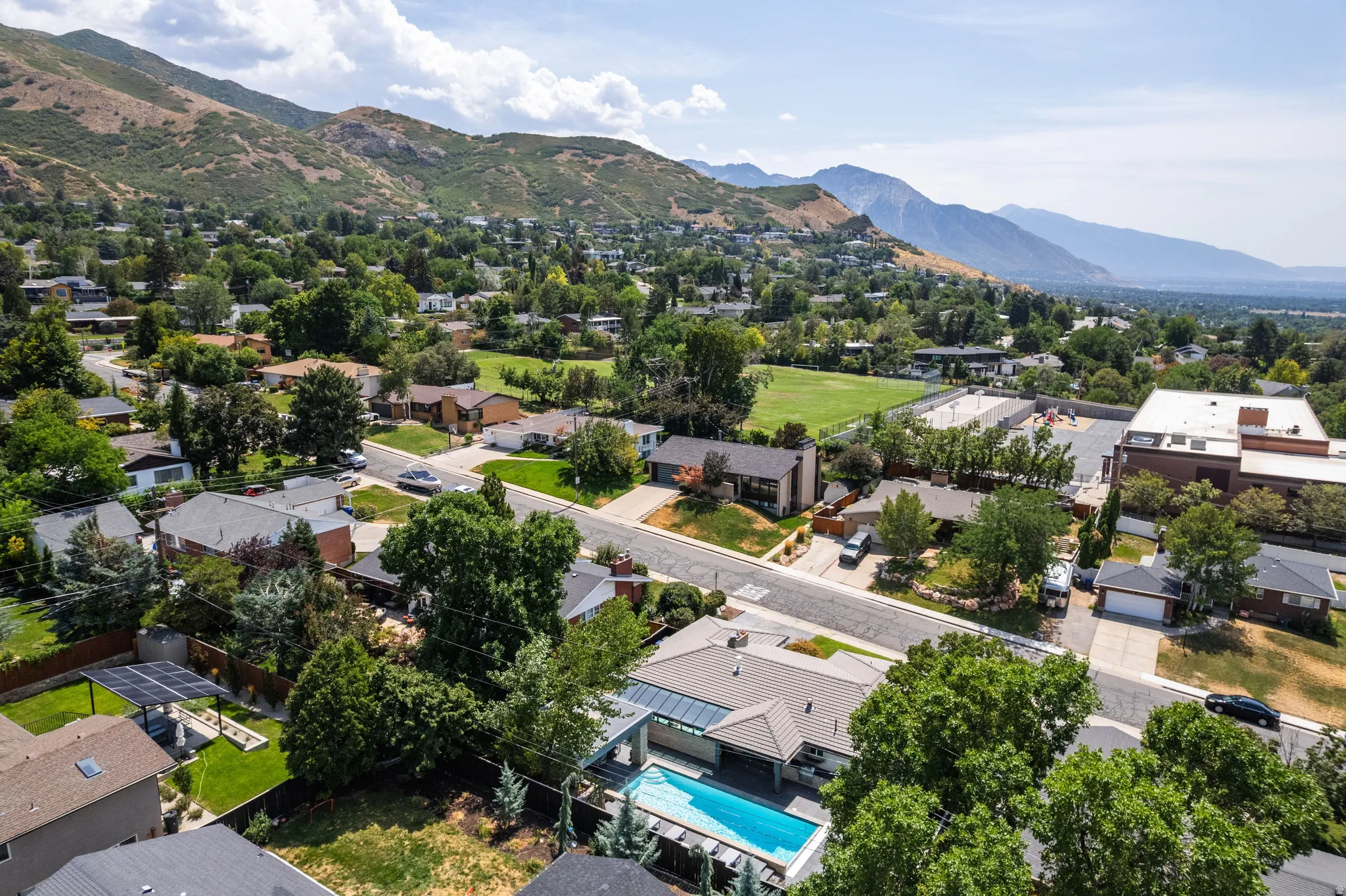 Expansive mountain backdrop with a residential setting, featuring a visible swimming pool, solar panels, and mature trees