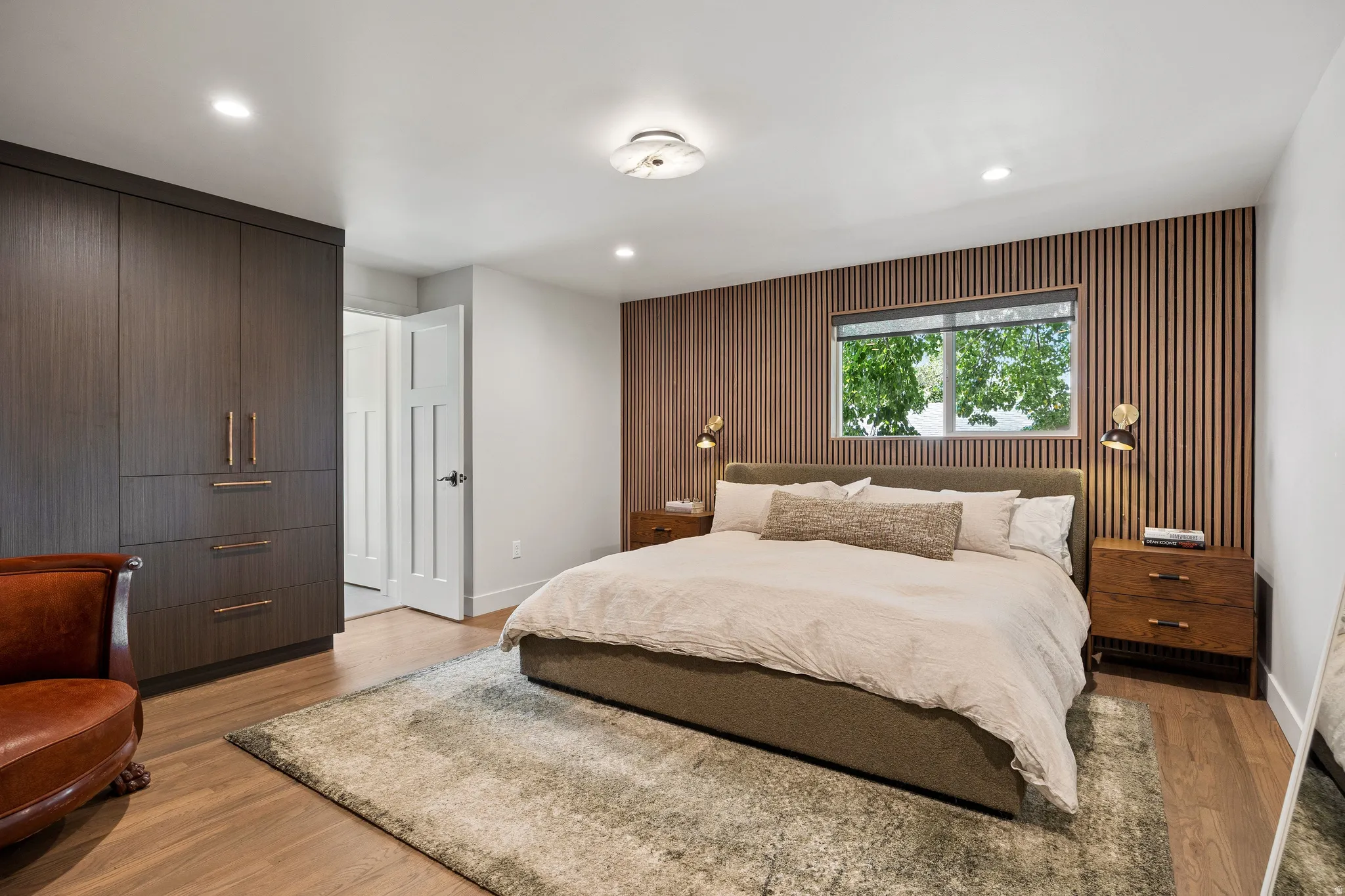 Wood-finish flooring, built-in dark wood cabinetry with bronze hardware, white interior door, slat wood-paneled accent wall, and recessed lighting