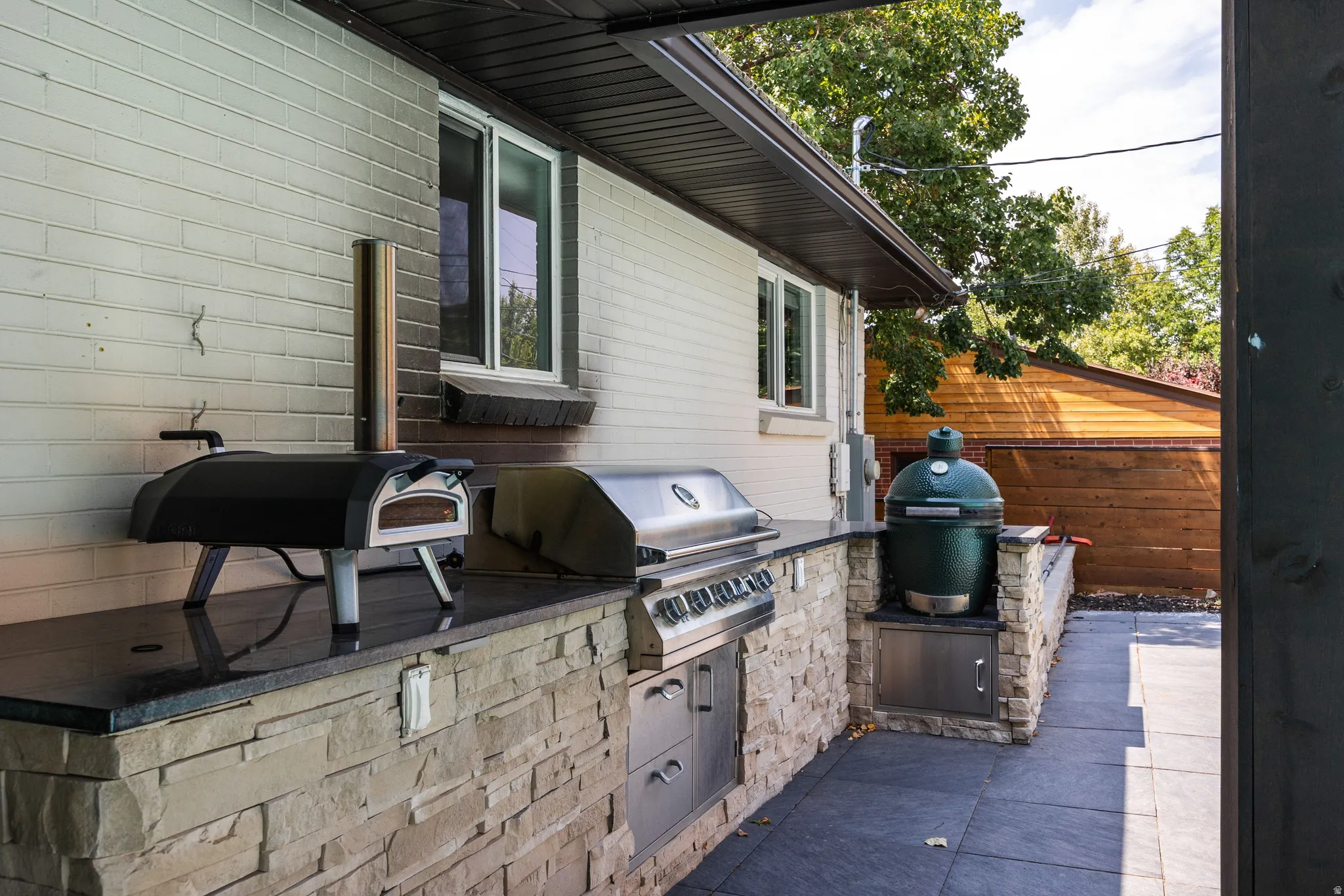 Outdoor kitchen featuring a built-in grill, stone veneer base, dark countertop, and a tiled patio surface