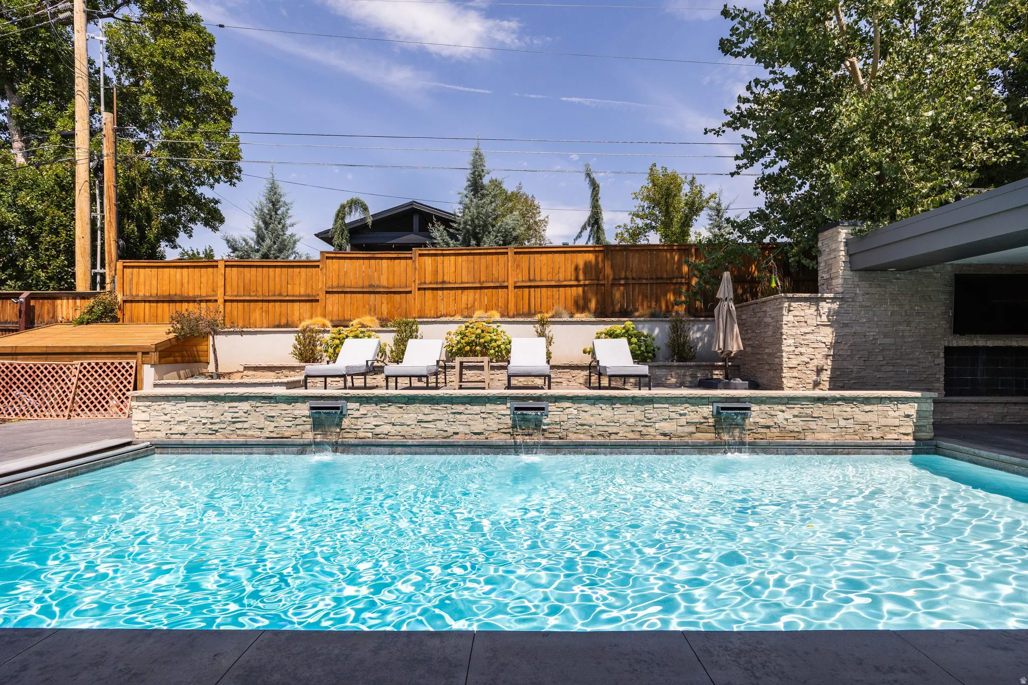 Swimming pool with multiple water features, stone-clad retaining wall, wood fencing, and a built-in outdoor entertainment area