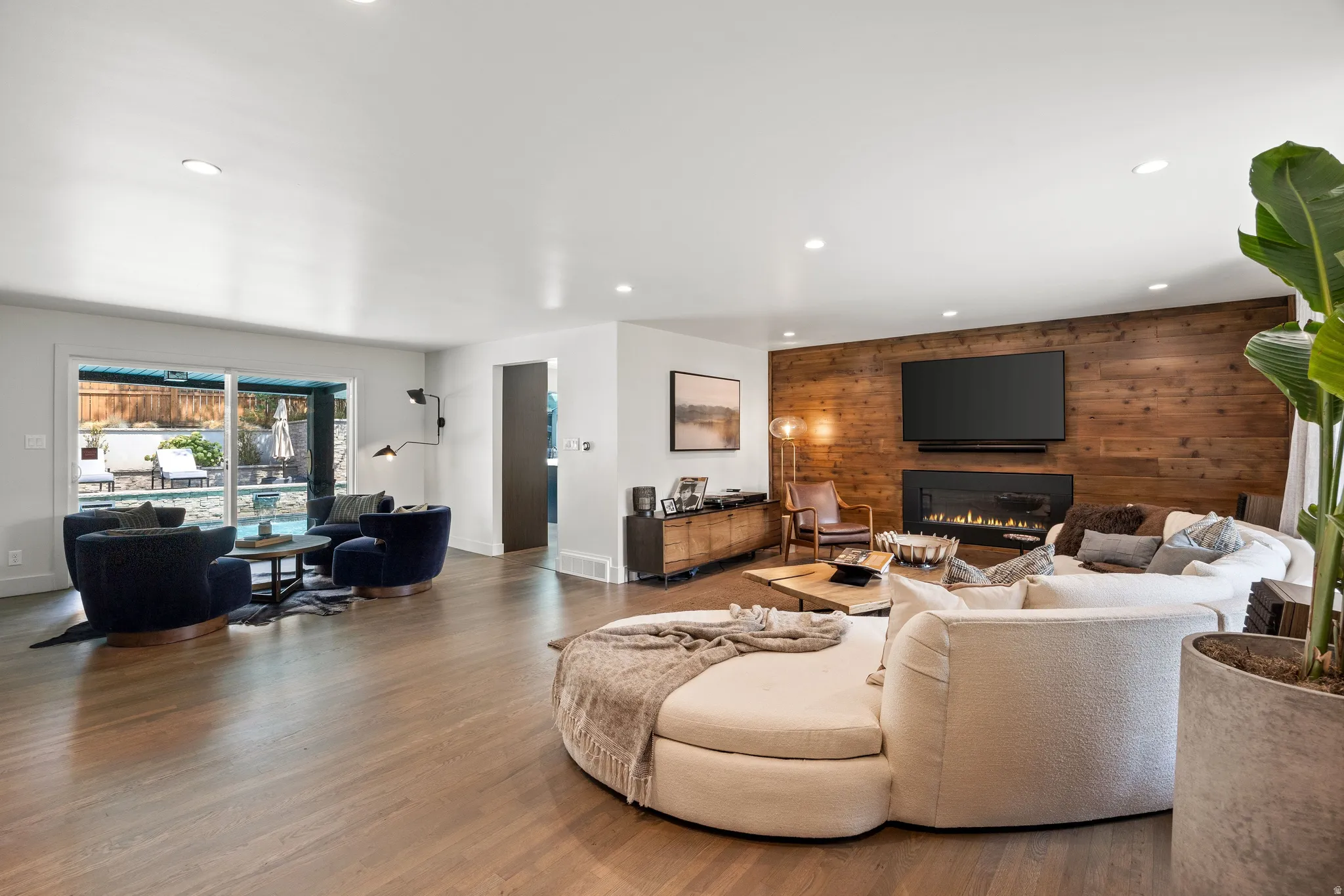 Recessed ceiling lighting, wood-finish flooring, a wood accent wall, built-in linear fireplace, and sliding glass doors