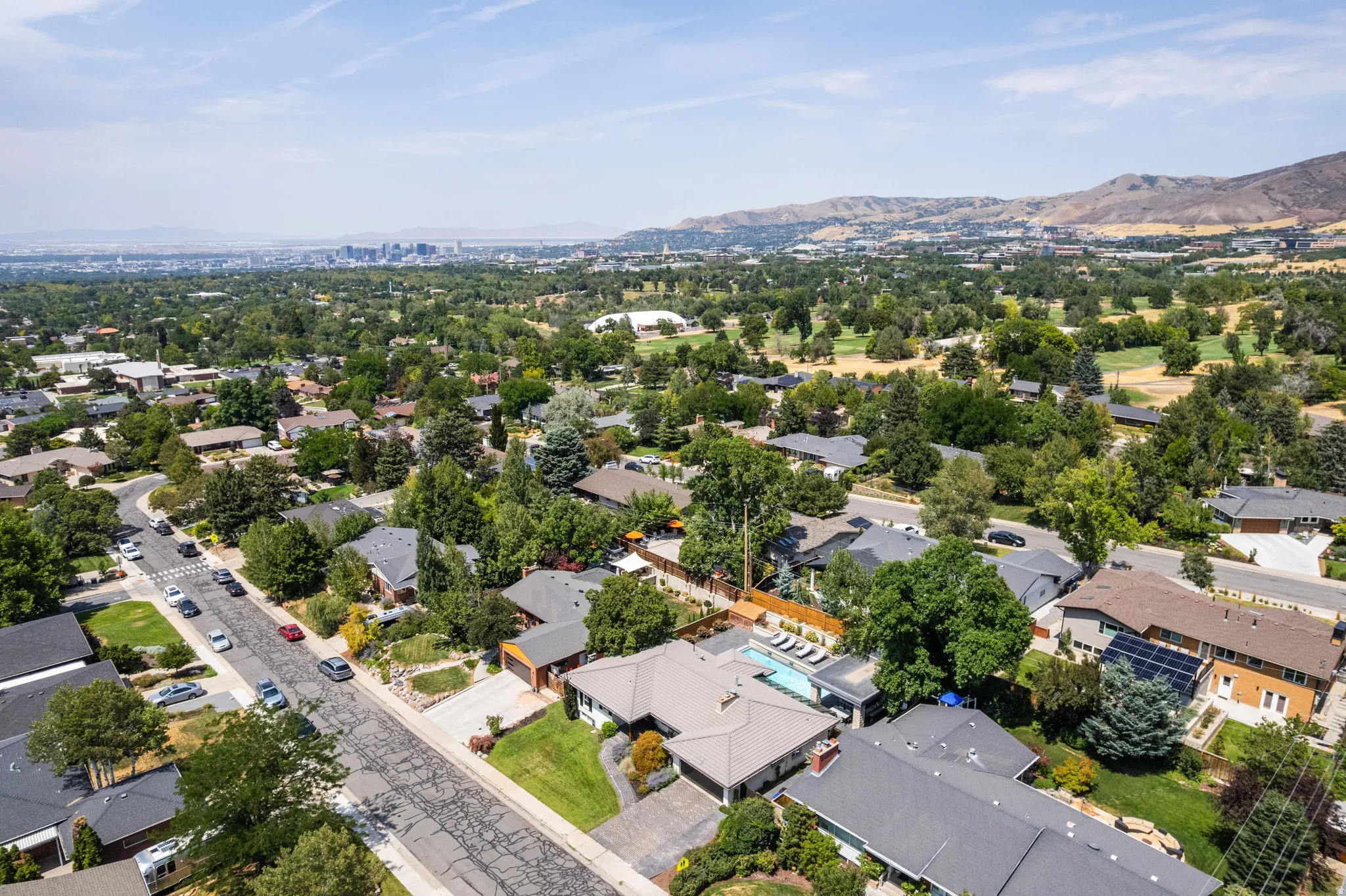 Aerial perspective showcasing a residential neighborhood with mature trees, established landscaping, and mountain backdrop
