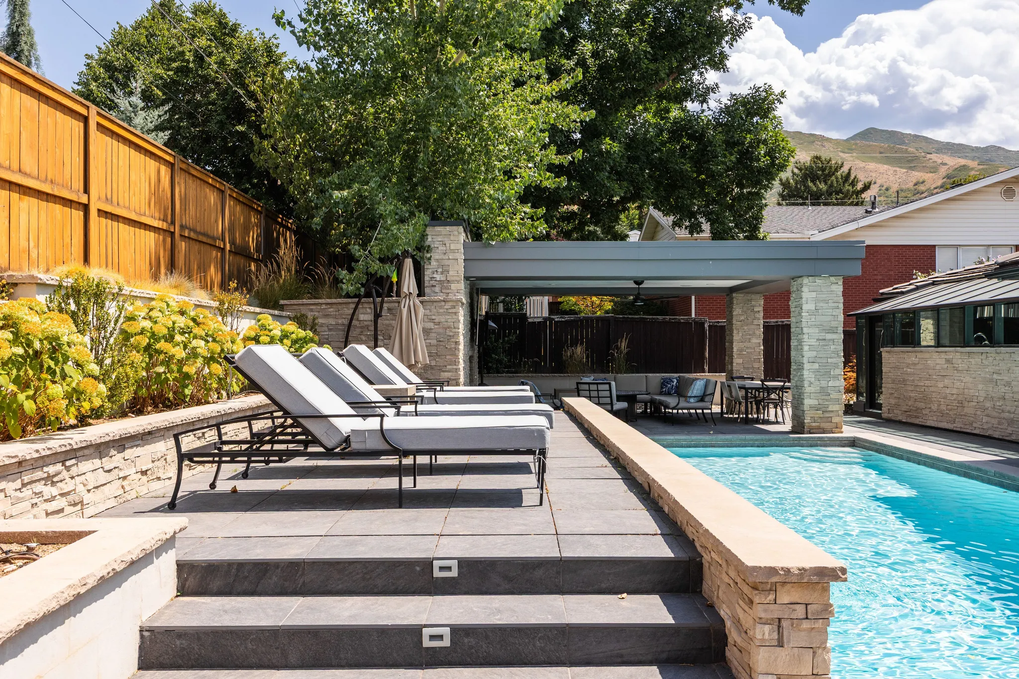 Expansive outdoor area featuring a swimming pool, integrated covered patio, stone-clad retaining walls, and a wood privacy fence