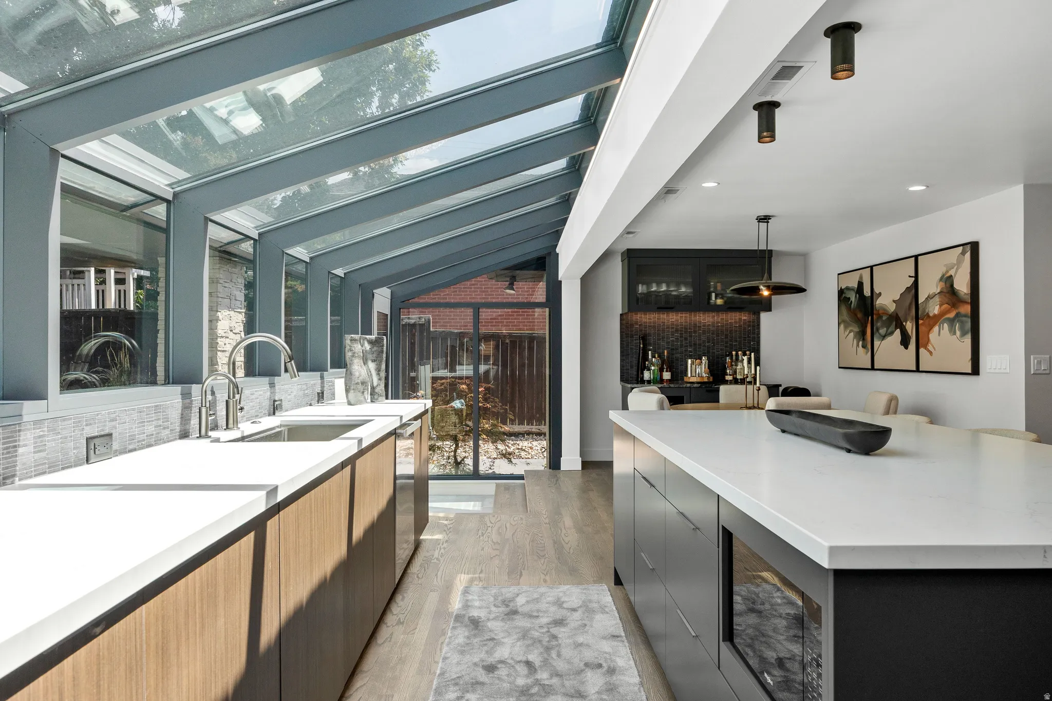 Expansive kitchen featuring a glass solarium extension, wood-finish cabinetry, a large kitchen island with integrated microwave, and a wet bar with a mosaic tile backsplash
