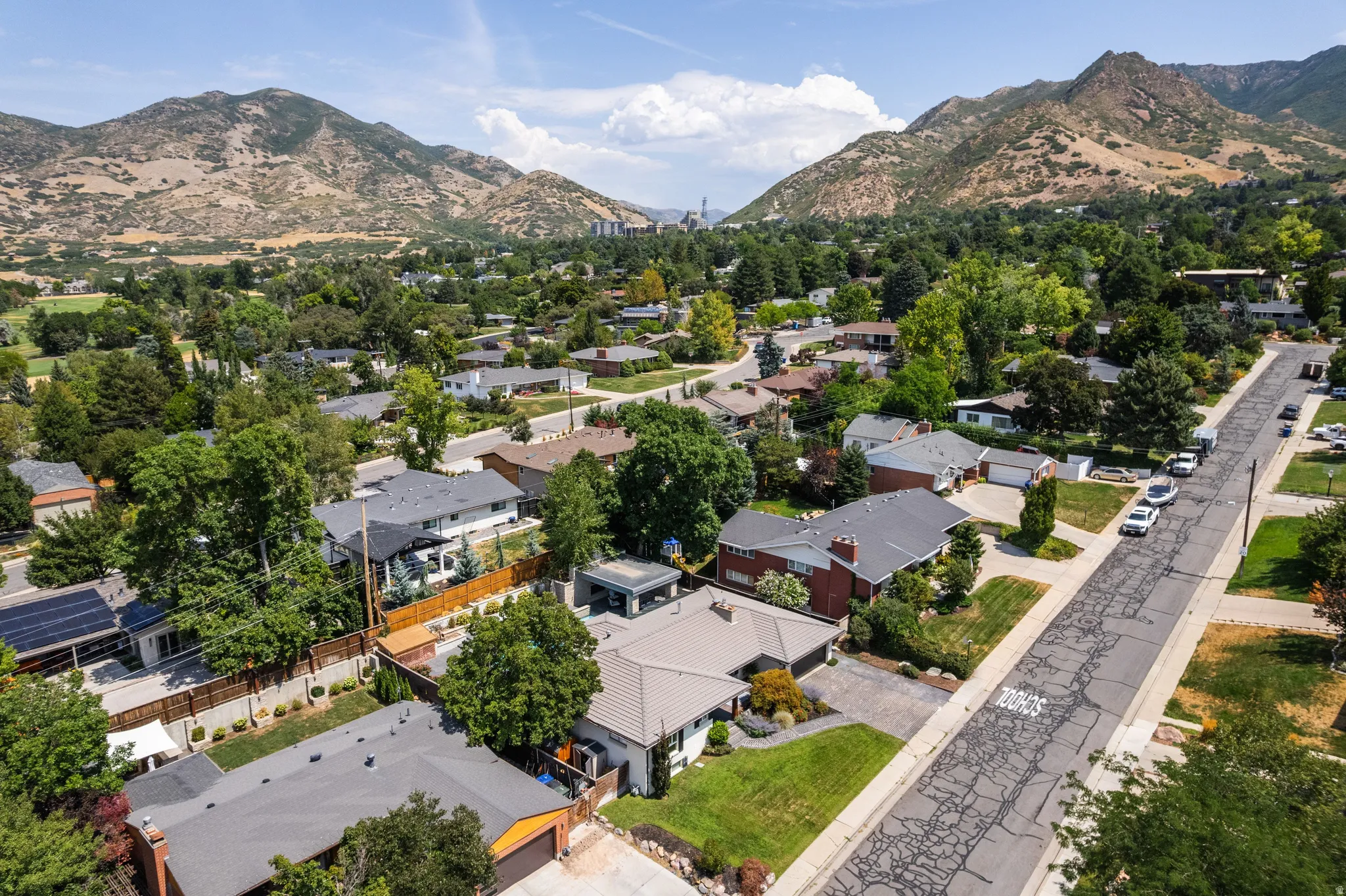 Residential area featuring a mix of mature trees, paved streets, and varied single-family homes, with a backdrop of mountains