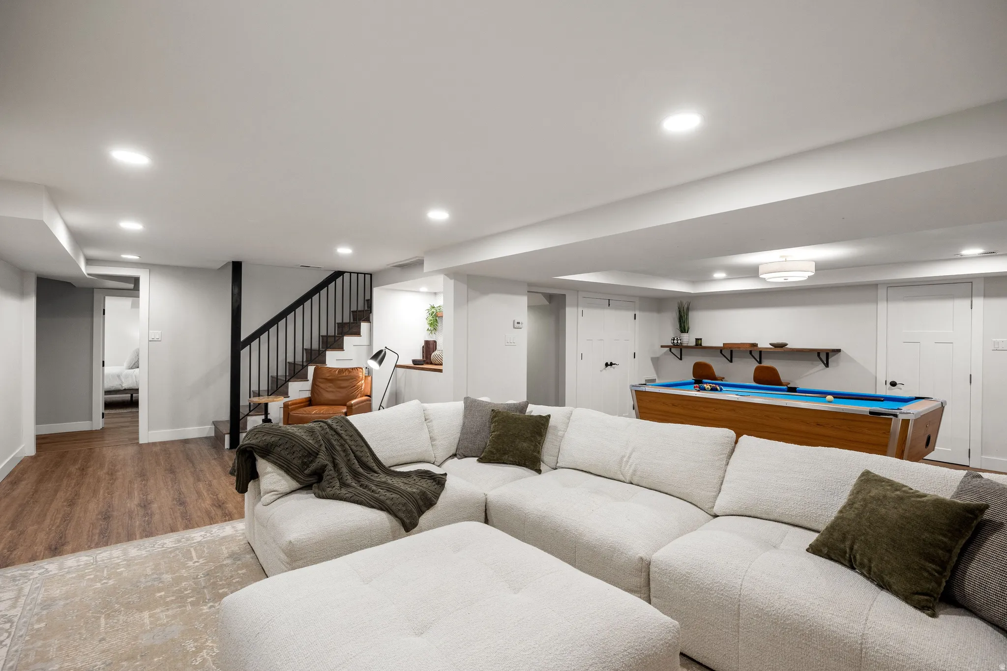 Finished lower level featuring recessed lighting, wood-finish flooring, a contemporary staircase with black railing, and white interior doors