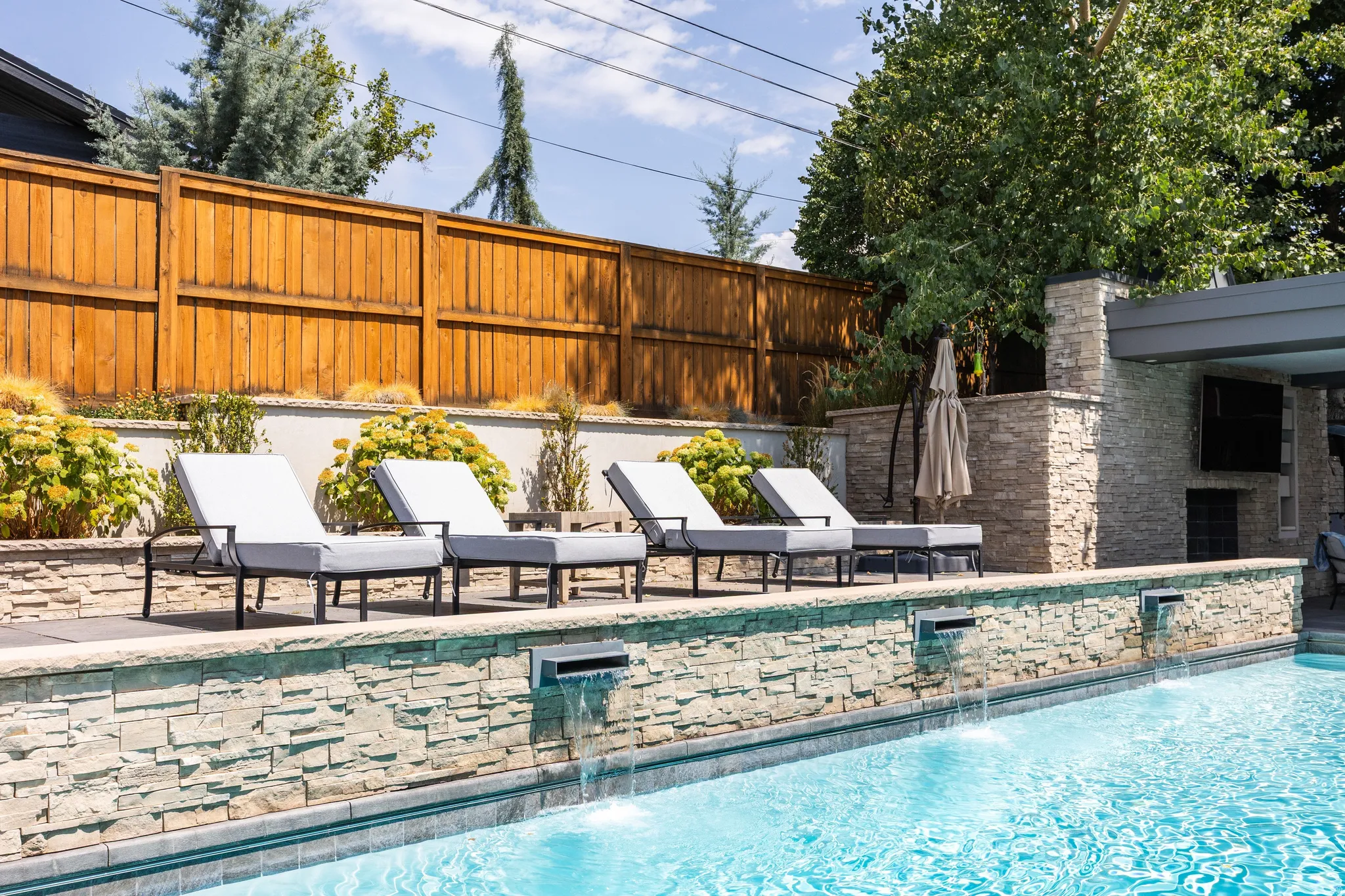 Swimming pool with integrated water features, stone-clad wall, and sun ledge with lounge seating