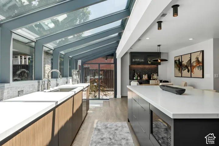 Expansive glass conservatory, integrated wet bar with dark tile backsplash, wood-finish flooring, white countertops, built-in microwave