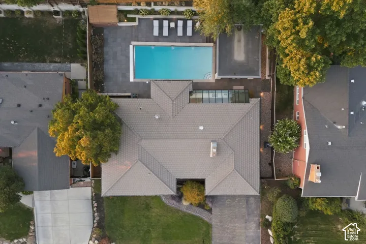 Aerial view showcasing a modern residence with a striking geometric roof design, resort-style swimming pool with turquoise water, manicured lawn, mature landscaping throughout the property, and neighboring homes framing the established residential setting