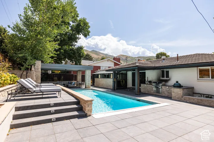 Outdoor swimming pool with integrated lighting, a covered patio area, and a built-in outdoor kitchen with stone accents