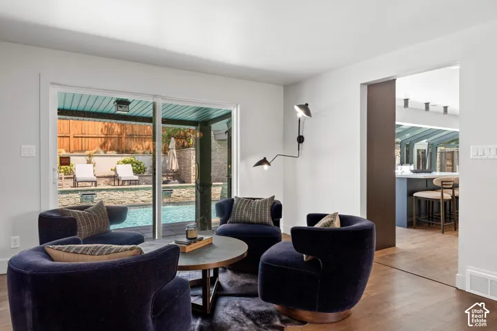 Sliding glass doors opening to an outdoor pool, wood-finish flooring, a wall-mounted articulating light fixture, a dark wood pocket door, and white baseboards