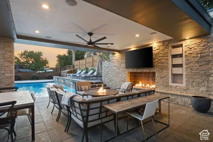Covered patio with integrated fireplace, stone accent wall, recessed lighting, ceiling fan, and swimming pool