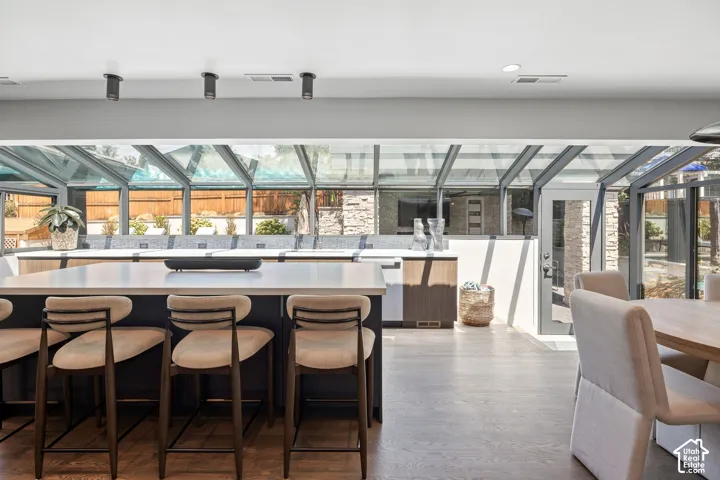 Modern kitchen and dining area featuring a waterfall-edge island with seating for three, white quartz countertops, stainless steel appliances, and abundant natural light from expansive glass panels overhead