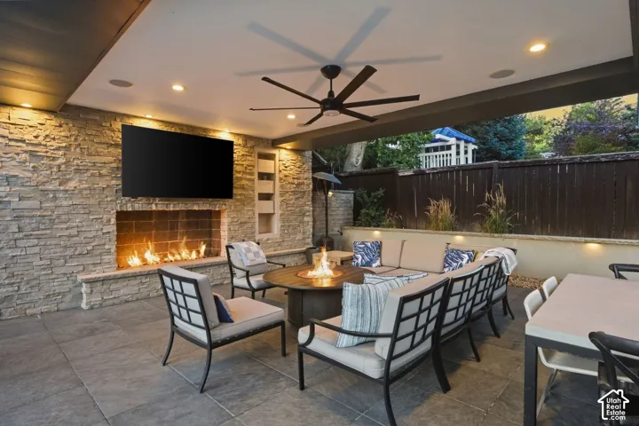 Covered patio featuring a stone-clad fireplace, integrated television, ceiling fan, and recessed lighting