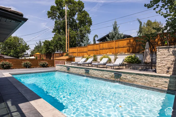 Swimming pool with stone-clad retaining wall, integrated water features, and a perimeter of dark paver decking