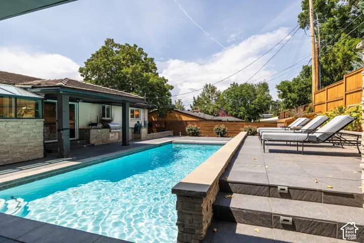 Outdoor pool with a stone retaining wall, tiled deck, and built-in outdoor kitchen