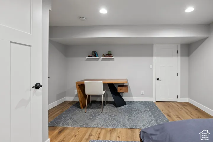 Finished basement office featuring warm wood-finish flooring, recessed ceiling lighting, and built-in wall shelving