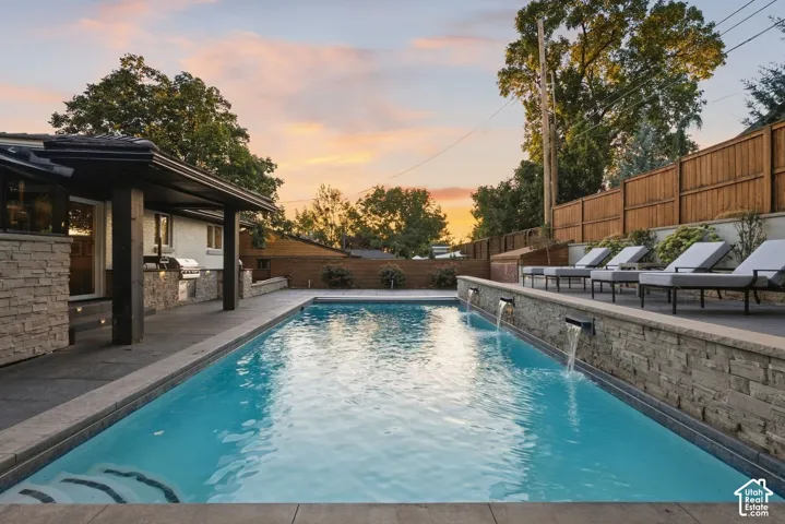 Rectangular swimming pool with integrated water features, a covered patio, and a stone-clad outdoor kitchen