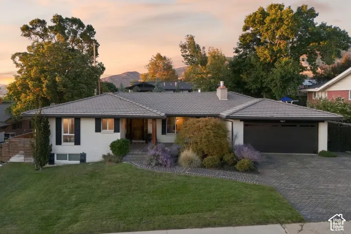 Paved driveway leading to an attached garage, mature landscaping, and a tiled roof