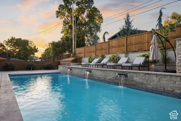 Rectangular swimming pool with stone waterfall features, concrete decking, and a wood privacy fence
