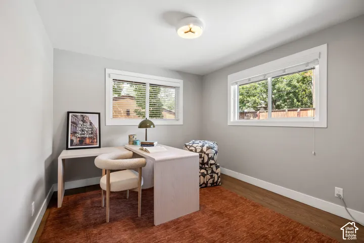 Recessed lighting illuminates a room featuring two windows with white blinds, wood-finish flooring, and light gray walls