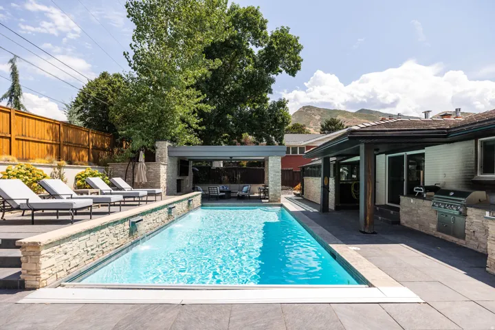 Outdoor swimming pool with integrated water features, expansive patio, covered outdoor living area, and built-in outdoor kitchen