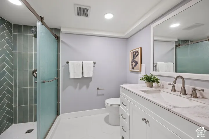 White hexagon tile flooring, a shower with herringbone tile, a sliding frosted glass shower door, a white vanity with an integrated sink, and a framed mirror
