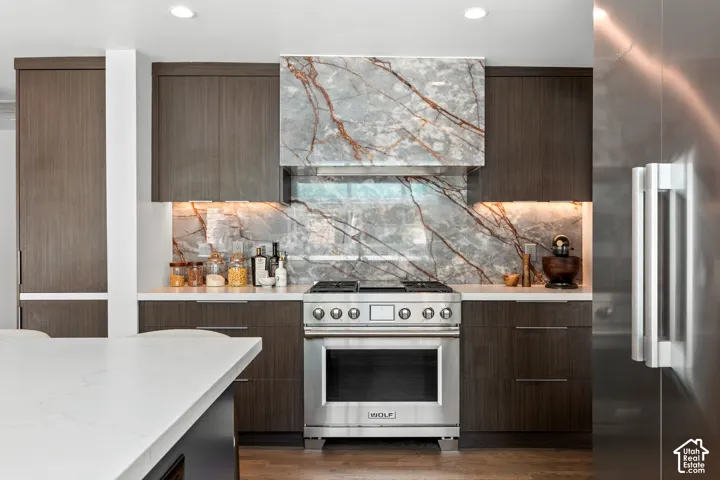 Kitchen featuring a stainless steel range, marble-finish backsplash, dark wood-finish cabinetry, built-in refrigerator, and recessed lighting