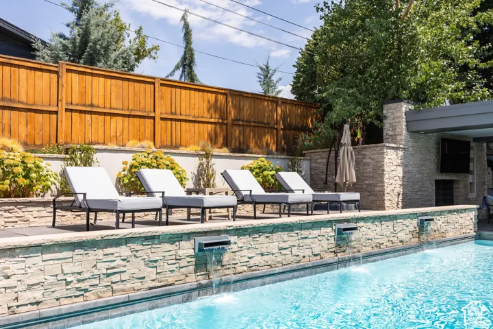 Swimming pool with stone-clad perimeter, multiple water features, and expansive paver decking