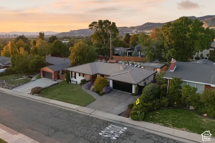 Pitched roofline with tile roofing, attached two-car garage, mature landscaping, paved driveway, and mountain backdrop