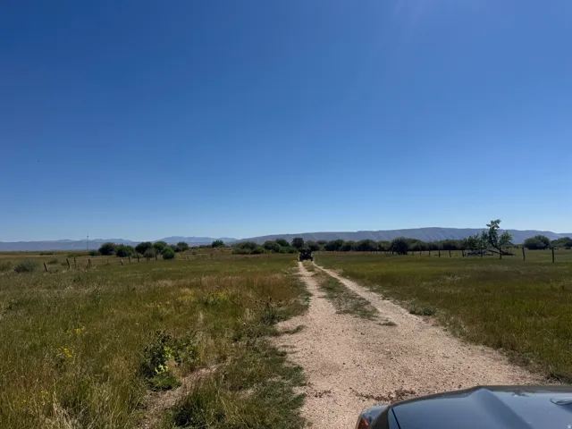 Expansive open land featuring a dirt road, natural fencing, and distant mountain ranges