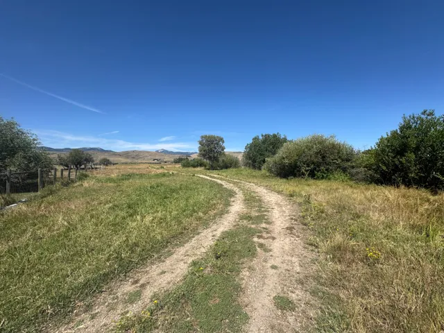 Expansive rural land featuring a natural dirt path, mature trees, and distant mountain topography
