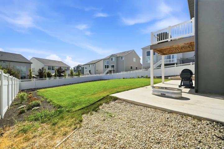 Expansive backyard featuring a manicured lawn, white privacy fencing, and a concrete patio with an overhead deck