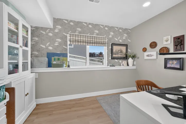 Recessed lighting, wood-finish flooring, built-in display cabinetry, window with privacy shade, and an accent wall with patterned wallpaper