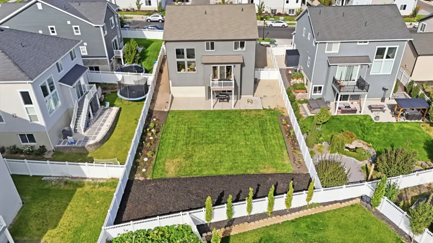 Expansive backyard featuring a large grass area, defined planting beds, and a white privacy fence