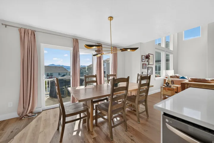 Open-concept dining area featuring wood-finish flooring, a modern linear chandelier, and a sliding glass door opening to an outdoor deck